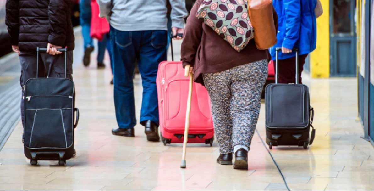 აეროპორტში ზურგით გადაღებული მგზავრები — მათ შორის ჭარბწონიანი ქალი ჩემოდნებით, რომელიც გამგზავრებისთვის ემზადება